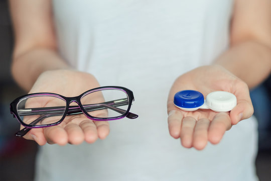 woman hold contact lenses and glasses in hands. concept of choice of vision protection