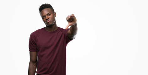 Young african american man with angry face, negative sign showing dislike with thumbs down,...