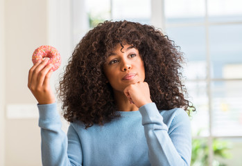 Fototapeta na wymiar African american woman holding donut at home serious face thinking about question, very confused idea