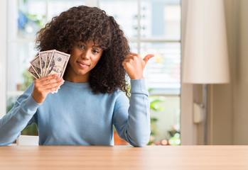 African american woman holding dollar bank notes pointing with hand and finger up with happy face...