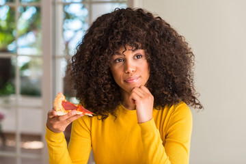 Fototapeta na wymiar African american woman ready to eat pepperoni pizza slice serious face thinking about question, very confused idea