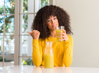 African american woman drinking healthy fruit juice at home pointing with hand and finger up with...