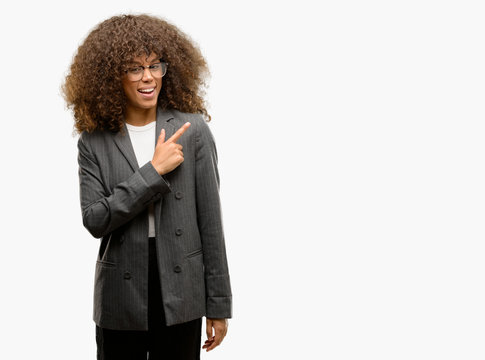 African american business woman wearing glasses cheerful with a smile of face pointing with hand and finger up to the side with happy and natural expression on face looking at the camera.