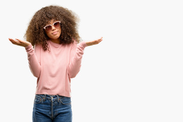 African american woman wearing pink sunglasses clueless and confused expression with arms and hands...