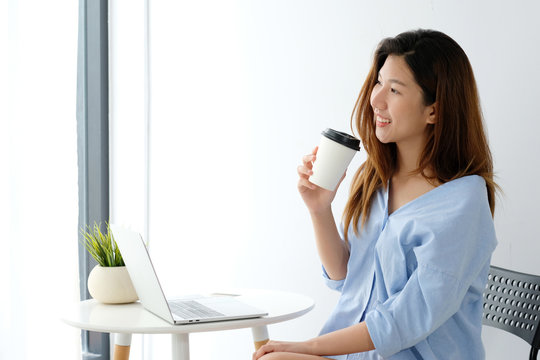 Young asian woman holding a coffee cup with smiling face, positive emotion at working desk background, casual office life, working from home concept