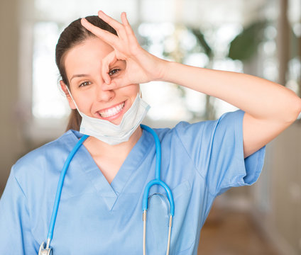 Young nurse woman wearing mask and stethoscope with happy face smiling doing ok sign with hand on eye looking through fingers