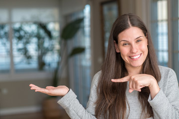 Young beautiful woman at home amazed and smiling to the camera while presenting with hand and...
