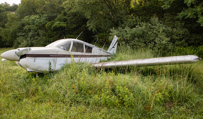 Old Single Engine Propeller Airplane in Overgrown Field with Trees in Background