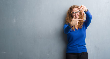 Young redhead woman over grey grunge wall smiling making frame with hands and fingers with happy face. Creativity and photography concept.