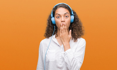 Young hispanic woman wearing headphones cover mouth with hand shocked with shame for mistake,...
