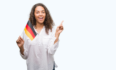 Young hispanic woman holding flag of Germany very happy pointing with hand and finger to the side