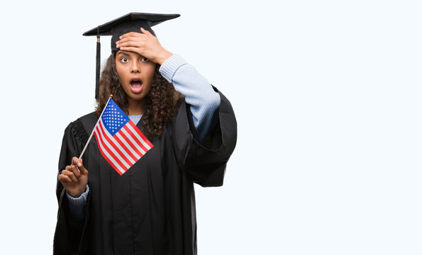 Young hispanic woman wearing graduation uniform holding flag of United States stressed with hand on head, shocked with shame and surprise face, angry and frustrated. Fear and upset for mistake.