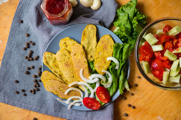 Crispy corn breads slices. Spicy and tasty on plate with green salad leaves, onion rings and tomatoes. Vegan lunch or vegetarian dinner. Healthy food concept.