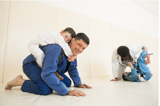 Male karate instructors training little children boys in dojo or jiu-jitsu at gym at tatami. Trainer teaches kid the basics of fighting for self-defense. Group of man and kids in sambo training