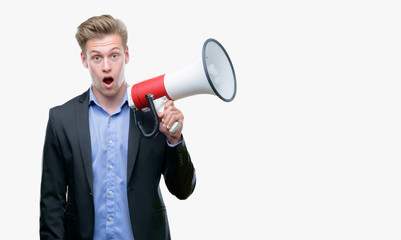 Young handsome blond man holding a megaphone scared in shock with a surprise face, afraid and excited with fear expression