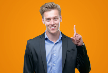 Young handsome blond business man surprised with an idea or question pointing finger with happy...