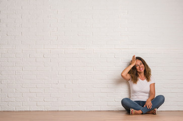 Middle age hispanic woman over white brick wall stressed with hand on head, shocked with shame and surprise face, angry and frustrated. Fear and upset for mistake.