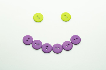 Purple and green buttons forming a smiley face on white background