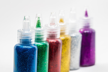Colorful bottles filled with glitter glue on white background.