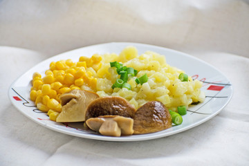 Fried potatoes with cepes and corn in a plate on the table. Fried potatoes with pickled mushrooms and corn.