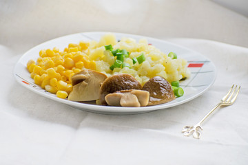 Fried potatoes with cepes and corn in a plate on the table. Fried potatoes with pickled mushrooms and corn.