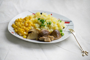 Fried potatoes with cepes and corn in a plate on the table. Fried potatoes with pickled mushrooms and corn.