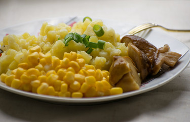 Fried potatoes with cepes and corn in a plate on the table. Fried potatoes with pickled mushrooms and corn.