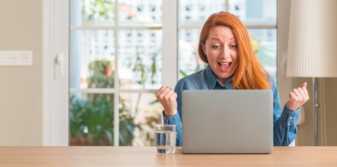 Redhead woman using computer laptop at home screaming proud and celebrating victory and success...