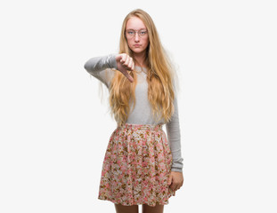 Blonde teenager woman wearing flowers skirt looking unhappy and angry showing rejection and negative with thumbs down gesture. Bad expression.