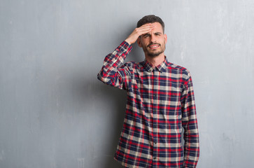 Fototapeta premium Young adult man standing over grey grunge wall stressed with hand on head, shocked with shame and surprise face, angry and frustrated. Fear and upset for mistake.