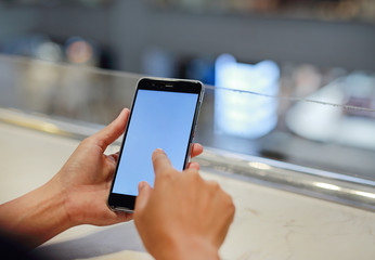 woman holding and using smartphone with blank white screen in cafe.