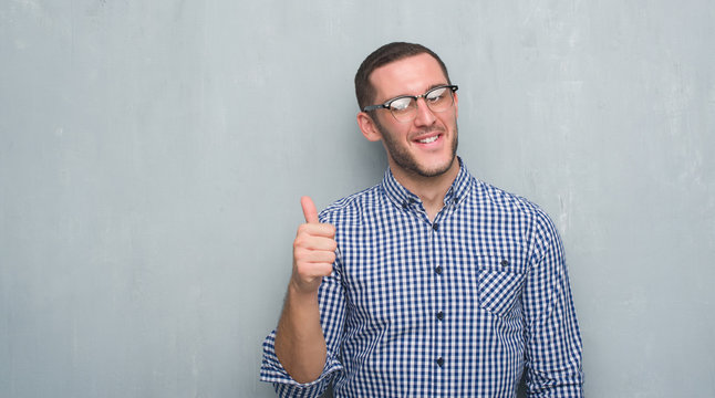 Young caucasian business man over grey grunge wall happy with big smile doing ok sign, thumb up with fingers, excellent sign
