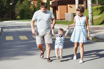 Young happy family: father, mother and blond boy walking in the park.