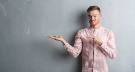 Young redhead man over grey grunge wall very happy pointing with hand and finger