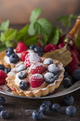  Dessert tarts with raspberries and blueberries on a wooden table.