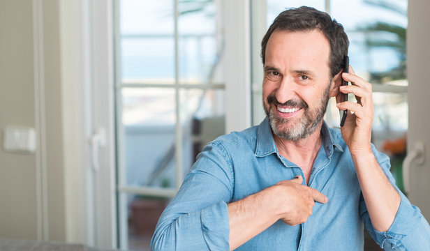 Middle age man using smartphone with surprise face pointing finger to himself