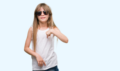 Young blonde toddler wearing sunglasses with surprise face pointing finger to himself