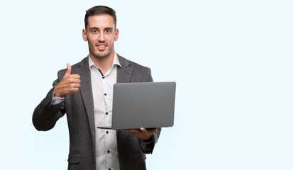 Handsome young man using computer laptop happy with big smile doing ok sign, thumb up with fingers, excellent sign