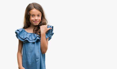 Brunette hispanic girl wearing denim dress pointing and showing with thumb up to the side with happy face smiling