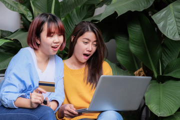 Two asia woman excited with sale promotion on website shop on laptop sitting on chair in garden at...
