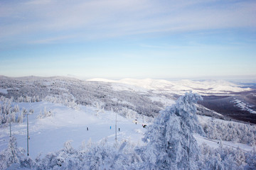 Winter landscape, snowy Ural mountains in cloudy day, trees in frost, ski center in the background