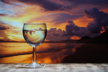 A glass of drinking water is on a wooden table against the background of the sea sunset.