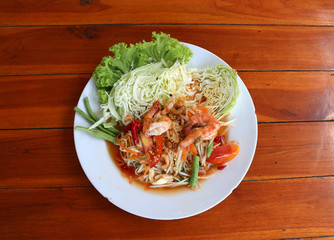 papaya salad with shrimp and vegetables, cabbage and yardlong bean in white dish on the wooden table.