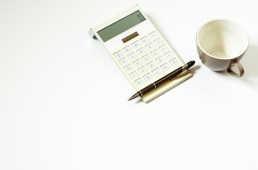 Weißer Taschenrechner mit Stift und Tasse auf weißem Hintergrund im Büro