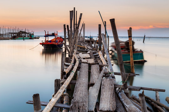 Old wood bridge for small fishing boat in the sea with sunset
