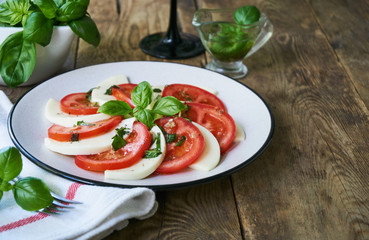 Italian salad with tomatoes, mozzarella and basil leaves on a grey plate