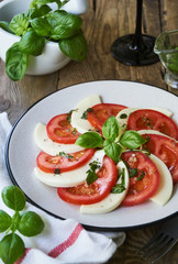 Italian salad with tomatoes, mozzarella and basil leaves on a grey plate