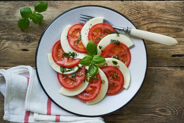 Italian salad with tomatoes, mozzarella and basil leaves on a grey plate