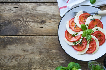 Italian salad with tomatoes, mozzarella and basil leaves on a grey plate