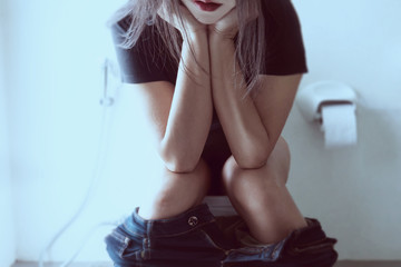 Woman sitting on toilet bowl holding tissue paper  - health problem concept
